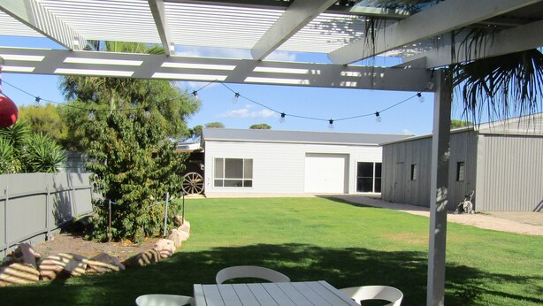 Un patio couvert avec une table et des chaises, une pelouse et un bâtiment en arrière-plan.