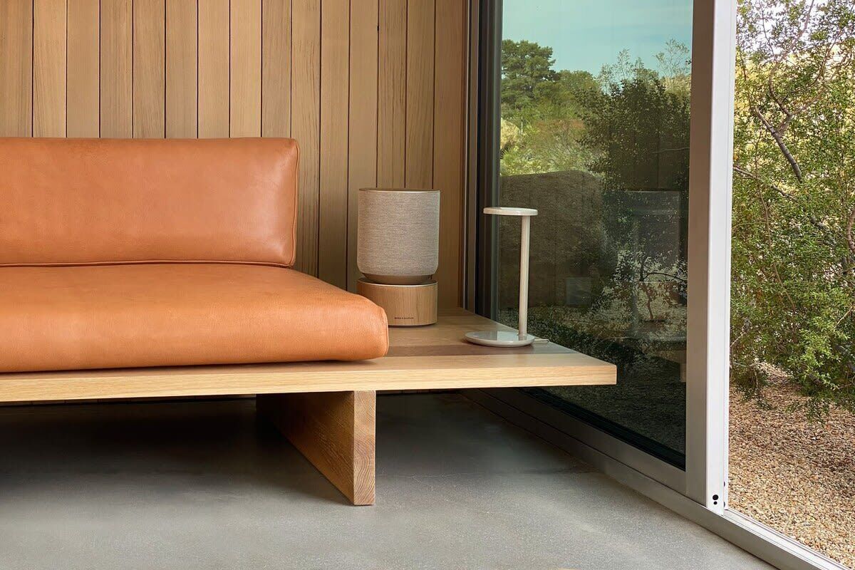 A modern room with a leather sofa, a lamp, and a view of greenery through a large window.