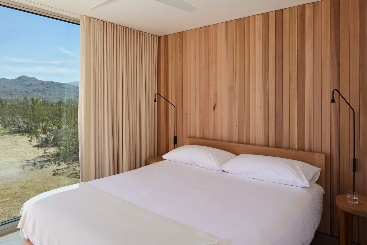 Ein Schlafzimmer mit einem großen Bett, Holzwandverkleidung, Blick auf eine Wüstenlandschaft und zwei Nachttischlampen.
