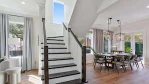 A modern interior with a staircase, dining area, and large windows. - Chic, Marigny Retreat | Heated Pool (New Orleans)