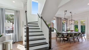 A modern interior with a staircase, dining area, and large windows. - Chic, Marigny Retreat | Heated Pool (New Orleans)