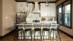 A modern kitchen with white cabinets, a central island with bar stools, a stainless steel refrigerator, and pendant lighting. - Chic, Marigny Retreat | Heated Pool (New Orleans)