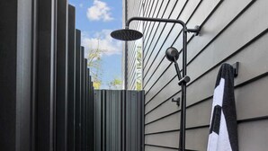 Un petit espace de douche extérieur avec une serviette noire accrochée au mur, une plante en pot et des toilettes.