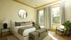 A bedroom with a bed, bedside tables, a large window with curtains, a round mirror, and a potted plant. - Chic, Marigny Retreat | Heated Pool (New Orleans)
