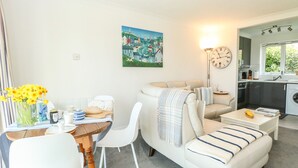 A modern living room with a sofa, a dining table, and a kitchen area visible through an open door. - Gull Cottage (Lowestoft)