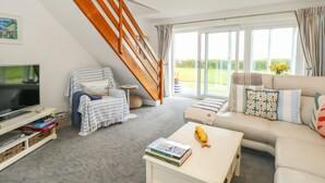 A living room with a TV, games, a sofa, a coffee table, and a staircase. - Gull Cottage (Lowestoft)