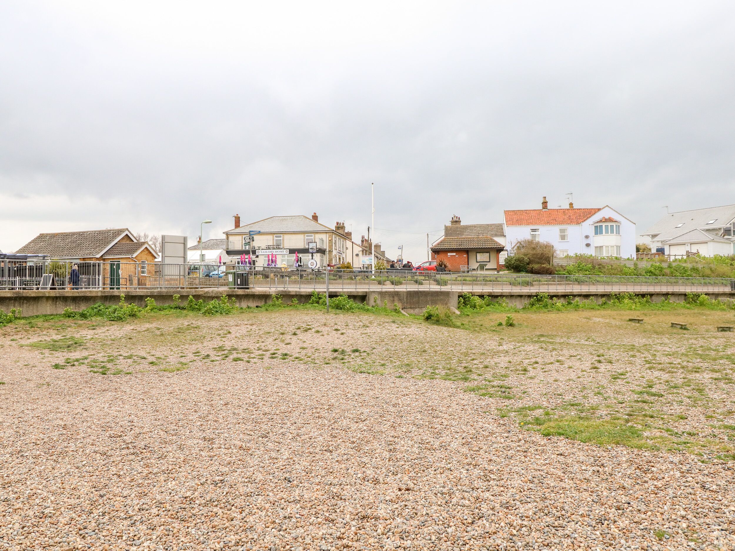 A coastal area with a pebbled beach, a pub named 'Sutton Home', and residential buildings.