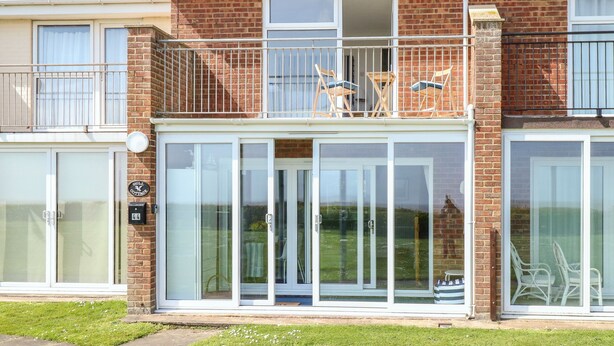 A two-story brick house with a balcony, large sliding glass doors, and a small garden area. - Gull Cottage (Lowestoft)