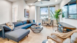 Una sala de estar moderna con un sofá modular, una mesa de centro, un mueble para televisor y un ventilador de techo.