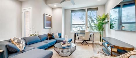 Een moderne woonkamer met een modulaire bank, een salontafel, een tv-meubel en een plafondventilator.