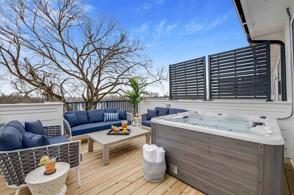 An outdoor deck with a hot tub, seating area, and a view of the sky.