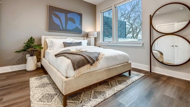 A bedroom with a bed, a large window, a wall-mounted mirror, and a piece of abstract art. - 4BR North Nashville Retreat | Rooftop Deck & Grill (Nashville)