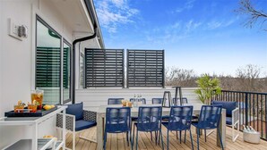 A deck with a table and chairs, a small bar cart, and a potted plant. - 4BR North Nashville Retreat | Rooftop Deck & Grill (Nashville)