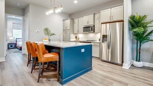 A modern kitchen with stainless steel appliances, a blue island, and a dining area with leather chairs. - 4BR North Nashville Retreat | Rooftop Deck & Grill (Nashville)