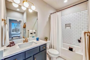 Features a large mirror, dual sink vanity, and separate toilet, plus a shower area with a tiled wall and curtain.