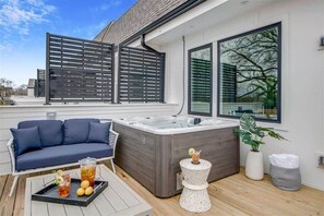 Relax in an outdoor oasis with a hot tub, comfortable seating, and a view of the surrounding trees.
