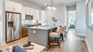 Una cocina moderna con armarios blancos, electrodomésticos de acero inoxidable y una isla central con asientos.