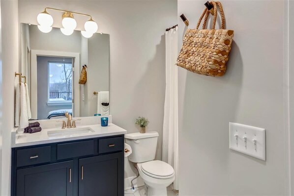 Un baño con lavabo, espejo, toallero, inodoro y una bolsa colgada.