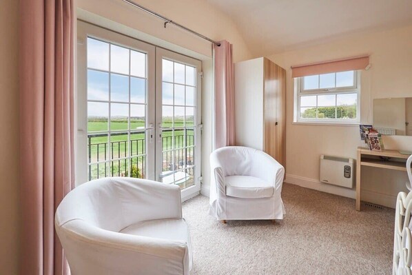 Relax in a comfortable space with a balcony overlooking a lush landscape, featuring a desk and armchairs.