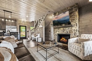 A spacious living area with a fireplace, a stone wall, and a large painting. A staircase leads to an upper level.