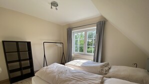 Un dormitorio con dos camas, una ventana con cortinas, un radiador y un armario negro.