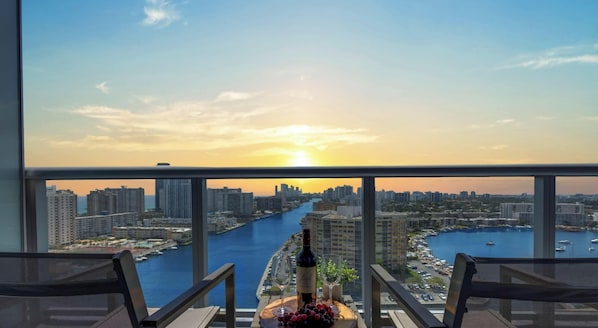 A balcony with a city view, a bottle of wine, and a fruit platter.