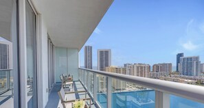 A balcony with a glass railing, a table with chairs, and a view of a cityscape with high-rise buildings.