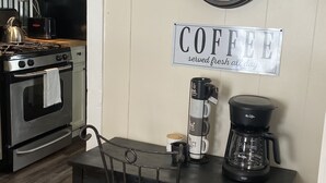 A kitchen with a clock, a coffee sign, and a coffee maker on the counter.