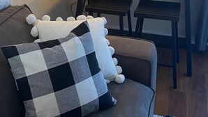 A cozy living room with a sofa, a checkered throw, a floor lamp, a wall clock, and a small wooden shelf.