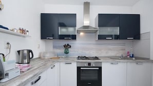 Una cocina moderna con armarios blancos, una campana de acero inoxidable, un horno empotrado y una encimera de mármol.