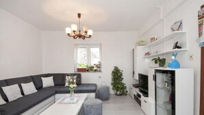 Una sala de estar moderna con un sofá seccional, una mesa de centro blanca, un aparador de vidrio y una televisión.