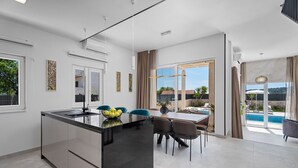 A modern kitchen with a central island, dining area with chairs, and a view of an outdoor swimming pool.