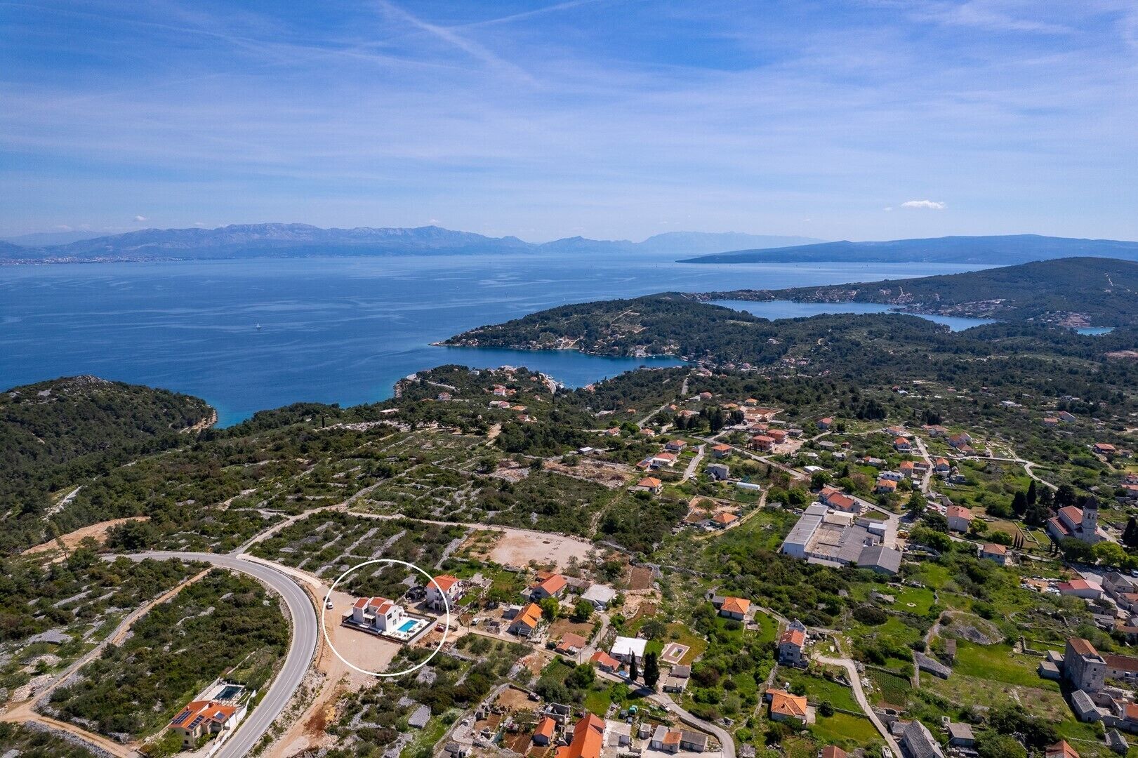 Vue aérienne d’un village côtier avec des maisons, une route sinueuse et une vaste étendue d’eau.