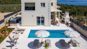 A modern two-story house with a swimming pool, outdoor seating, and a view of the sea.