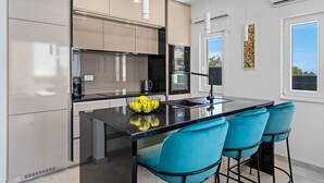 A modern kitchen with a black countertop, stainless steel appliances, and a bowl of lemons. There are three blue chairs at the island.