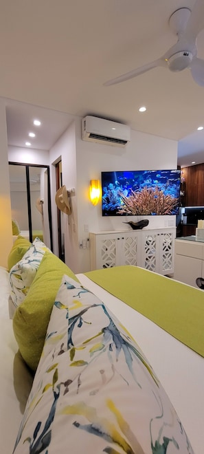 A modern living room with a flat-screen TV, a ceiling fan, and a white air conditioning unit.
