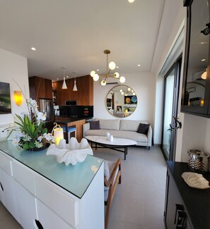 A modern kitchen with a central island, a dining area with a round table, and a living room with a sofa and a large mirror. - Blissful Ocean-View Penthouse with Rooftop Pool (Puerto Vallarta)
