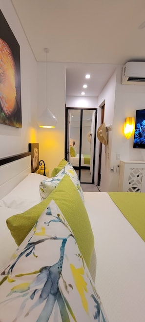 A hotel room with a bed, a bedside table, a lamp, a wall-mounted TV, and a door leading to a bathroom. - Blissful Ocean-View Penthouse with Rooftop Pool (Puerto Vallarta)