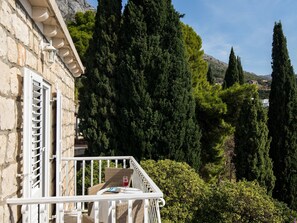 A balcony with wicker furniture and a glass of red wine, overlooking a mountainous landscape with tall trees. - Rooms Tupina by Paulina - Comfort Double Room With Balcony and Sea View (Zupa dubrovacka)