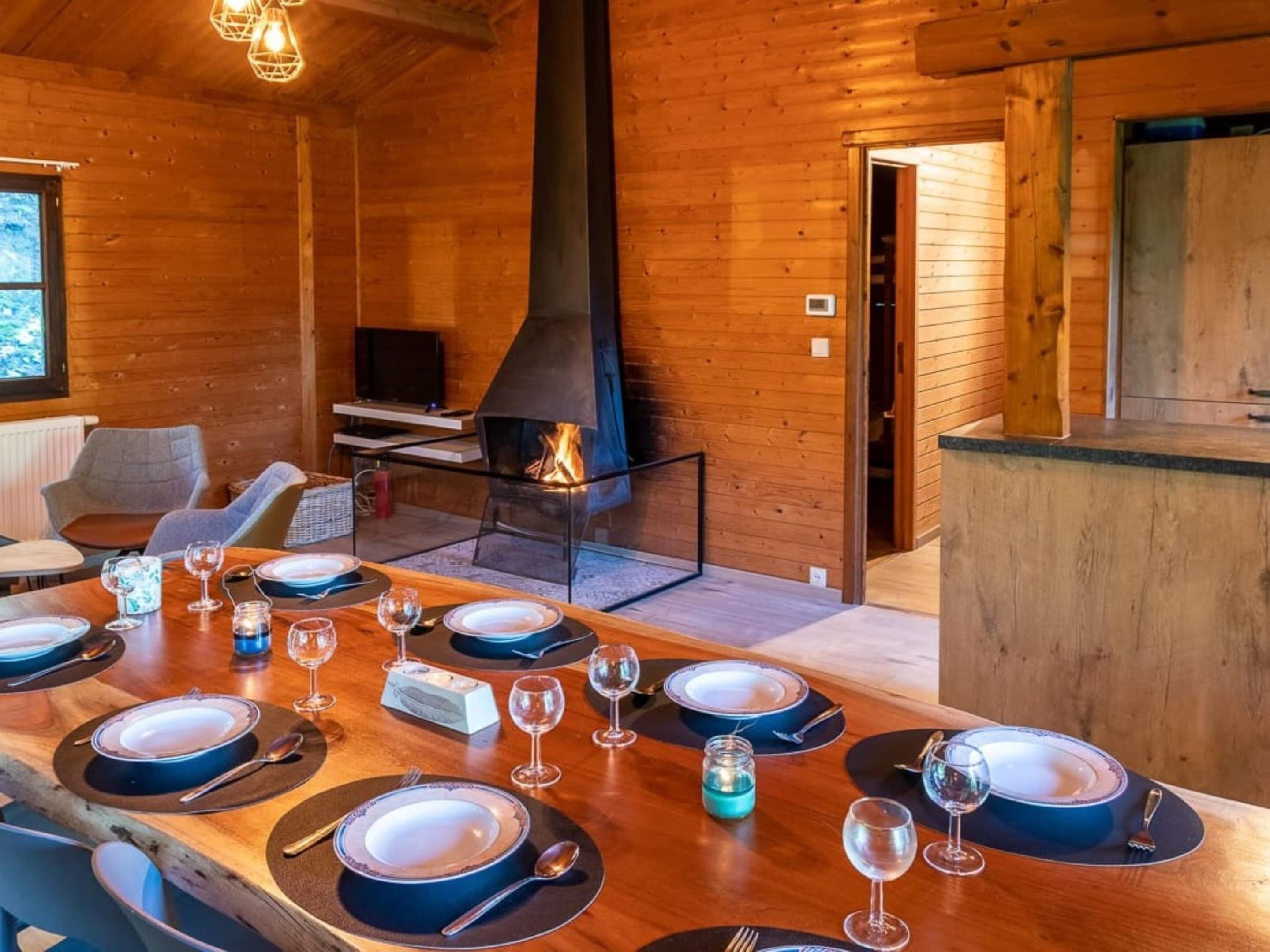 A wooden cabin interior with a dining table set for six, a fireplace, and a television.