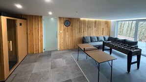 A modern room with a wooden wall panel, a dartboard, a sofa, and a foosball table. - Chalet in the Woods With Nordic Bath (Manhay)