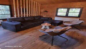 A cozy cabin interior with a dark leather sofa, a round coffee table, and a modern chair. - Chalet in the Woods With Nordic Bath (Manhay)