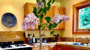 A kitchen with wooden cabinets, a stove, and a vase with flowers on a wooden table. - Redwood Creek Getaway! (Redway)