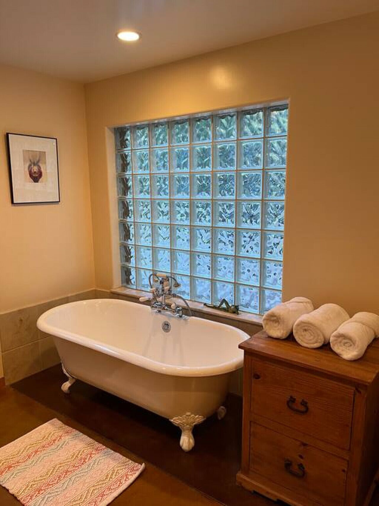 A bathroom with a freestanding bathtub, a wooden vanity with drawers, a patterned rug, and a window with frosted glass.