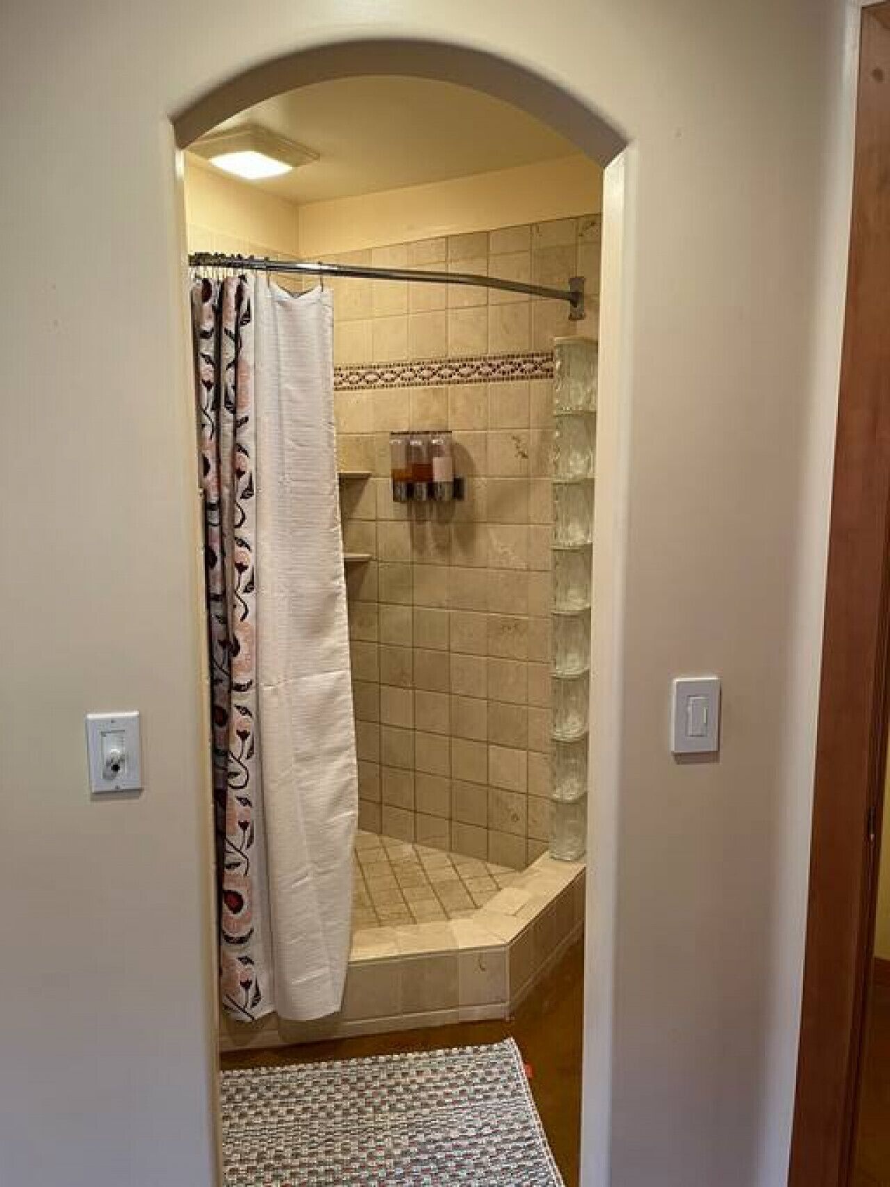 Una ducha con cortina estampada, paredes de azulejos y un pequeño estante con artículos de aseo.