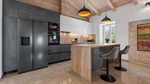 Une cuisine moderne dotée d’appareils électroménagers en acier inoxydable, d’un îlot central en bois et de luminaires suspendus.