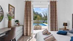 Une chambre avec vue sur une piscine, un bureau, une chaise, un lit avec des oreillers et une table de chevet avec une lampe.