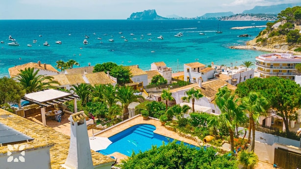Eine Küstenstadt mit einem Schwimmbad, umgeben von Palmen und Gebäuden im mediterranen Stil.