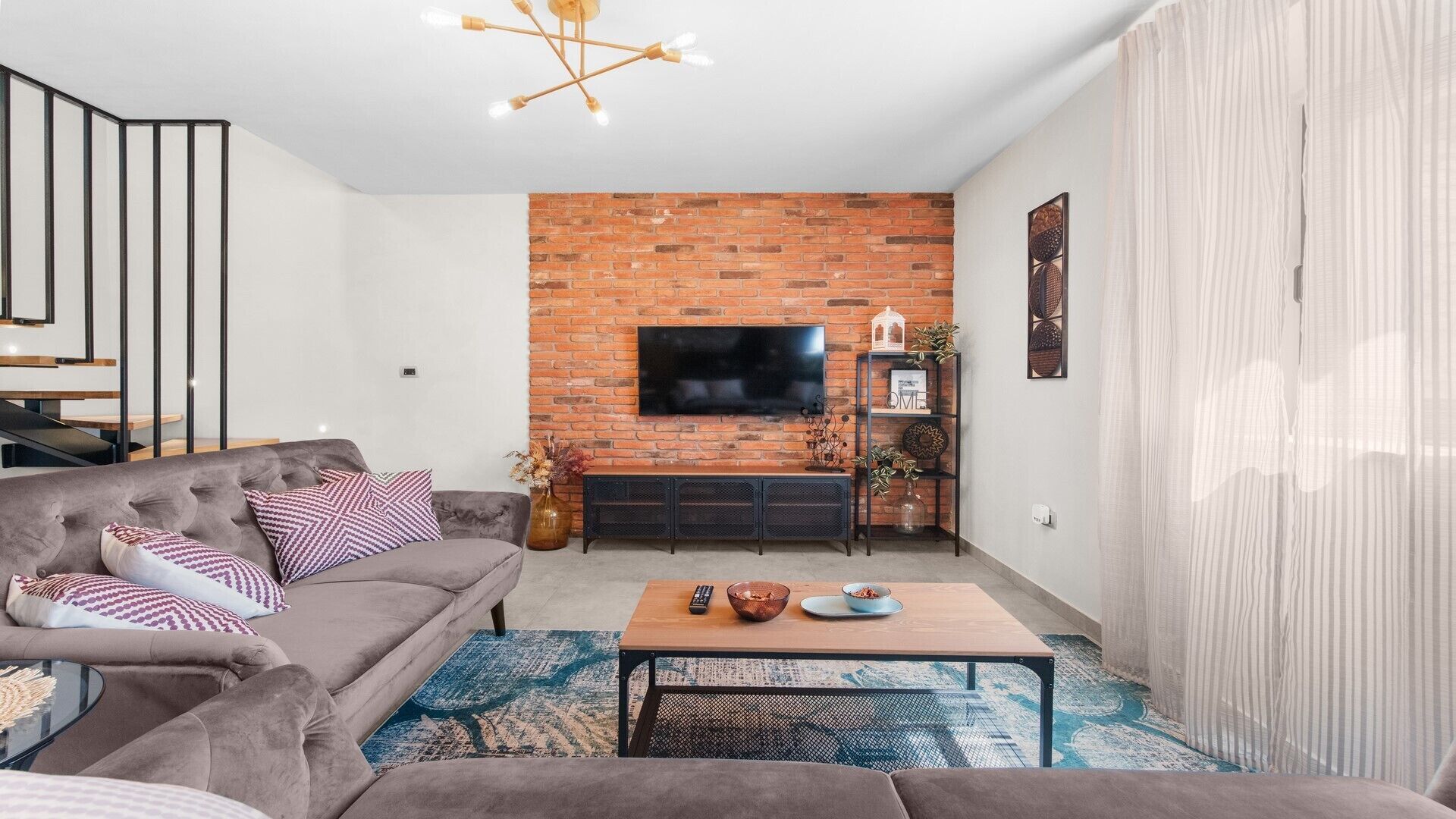 Una sala de estar moderna con pared de ladrillo decorativa, televisor de pantalla plana, sofá gris y una mesa de centro.