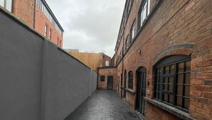 Une ruelle étroite bordée d’immeubles en briques, d’un mur gris et d’une clôture en bois.